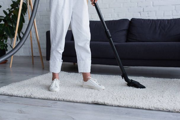 A woman is using a vacuum cleaner to clean a rug in a living room.