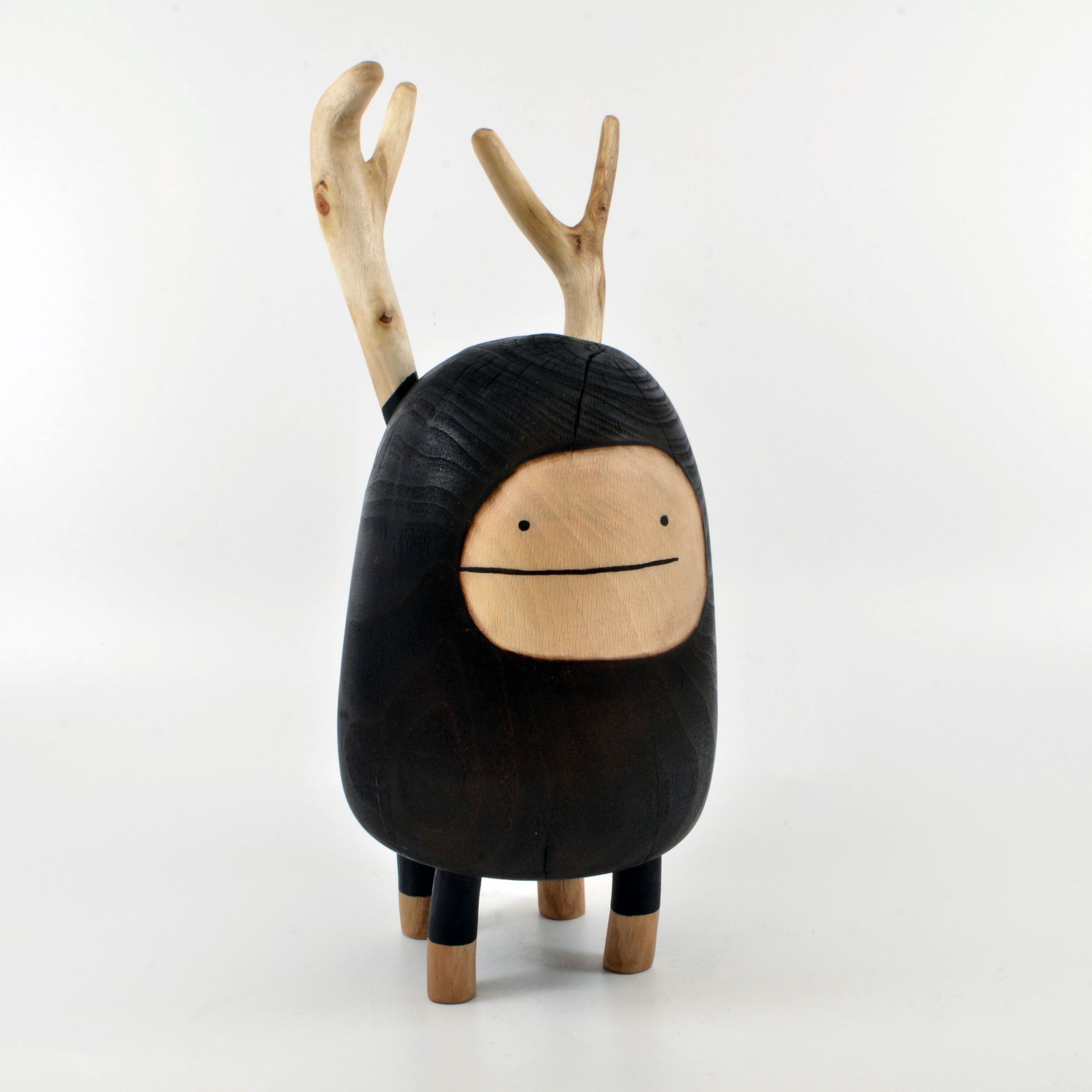 A wooden figurine with its body and simple face painted in black, and two antlers