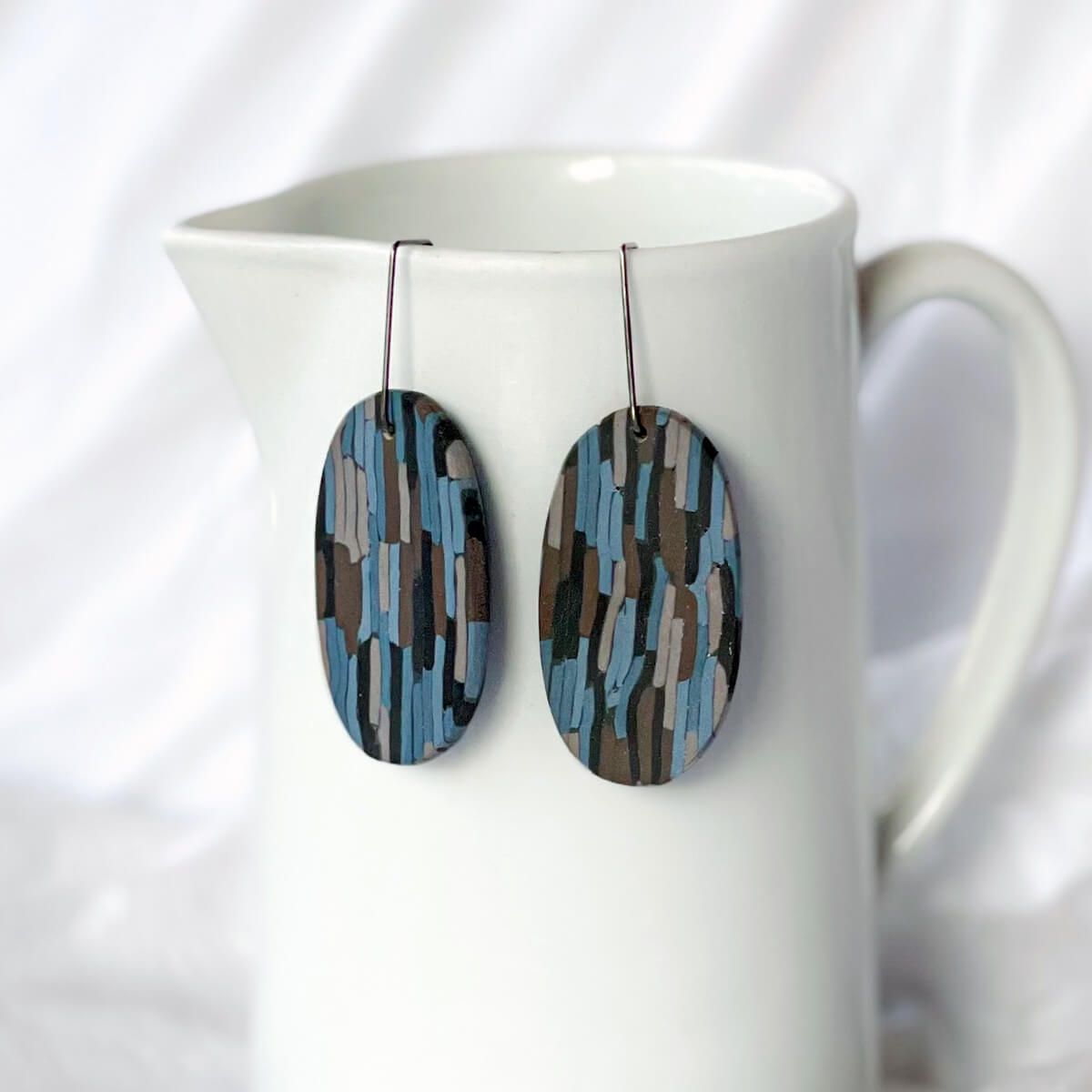 a pair of oval-shaped earrings speckled with brown, blue, black and beige colours