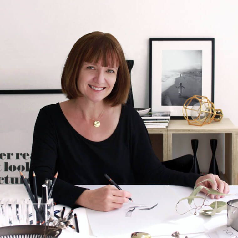 Nicole Henrickson sits at a table, drawing a sprig of gum leaves which are sitting on the table