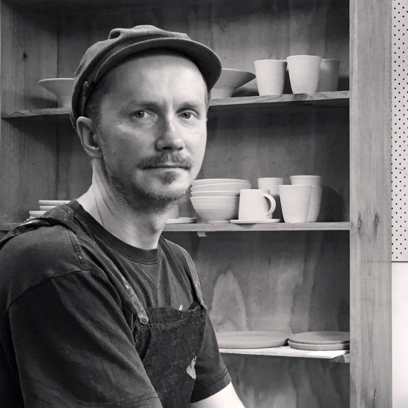 potter Rafel Kaczmarek of Sticky Earth sits in front of a shelf filled with his ceramic tableware