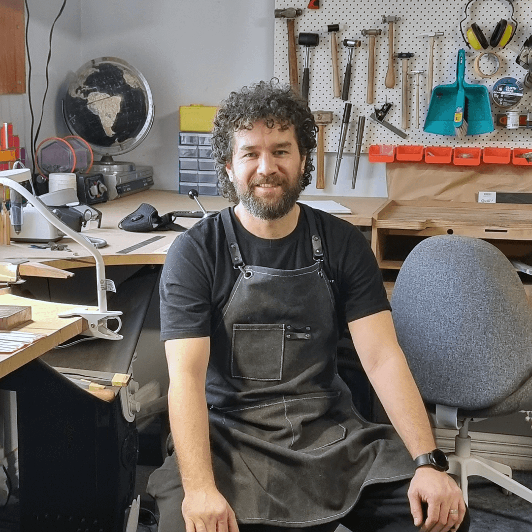 Ty Kouka, a jewellery maker, sits in a cluttered workshop