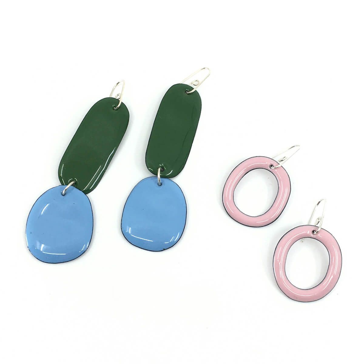 two pairs of enamel earrings in organic rounded shapes, one pair is dark green and sky blue, the other pair is pale pink