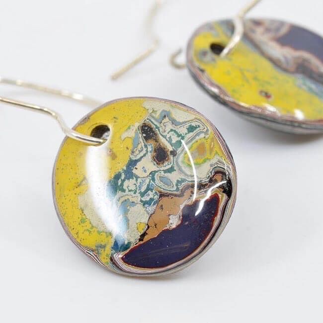 a pair of round hanging earrings made from graffiti paint chippings, resembling planet earth from space