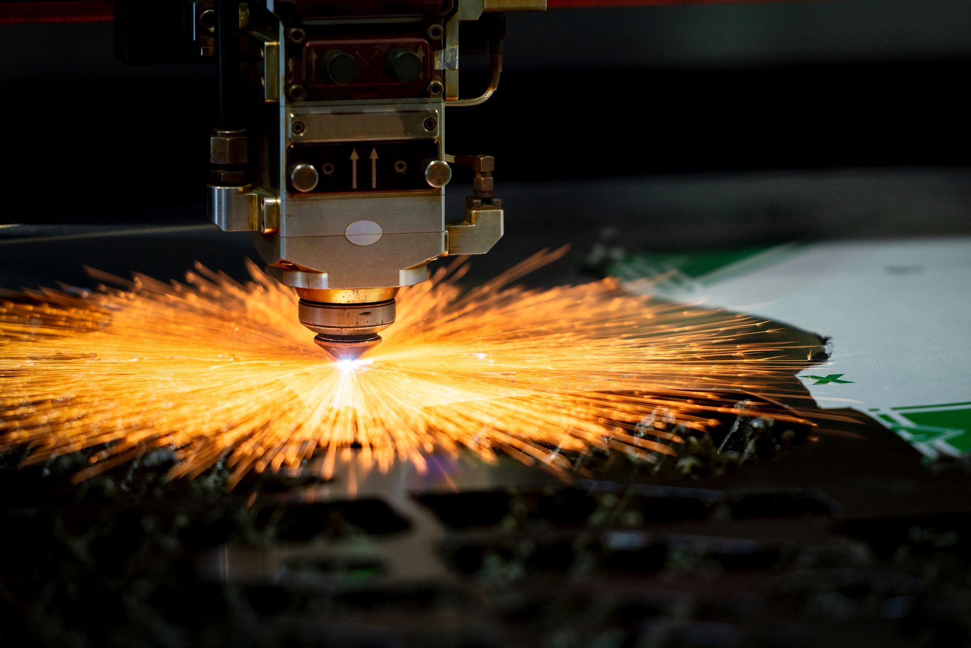 Laser cutter in operation, sparks flying from metal sheet.