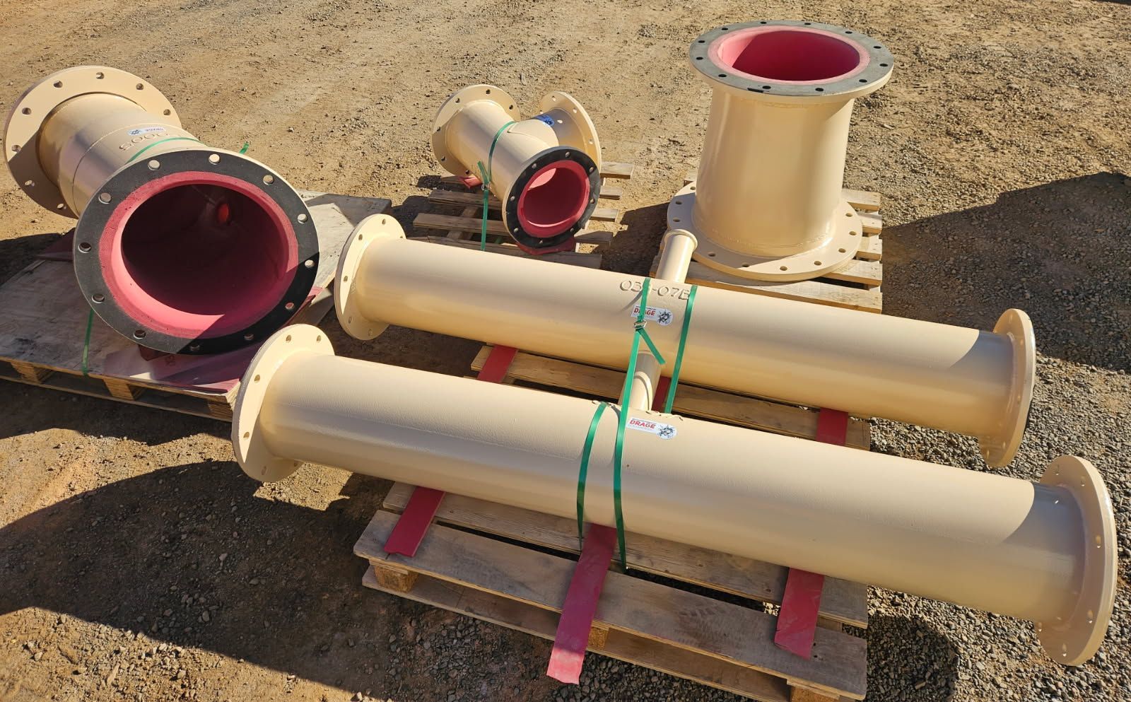 Tan pipes with pink interiors, on a wooden pallet outdoors.