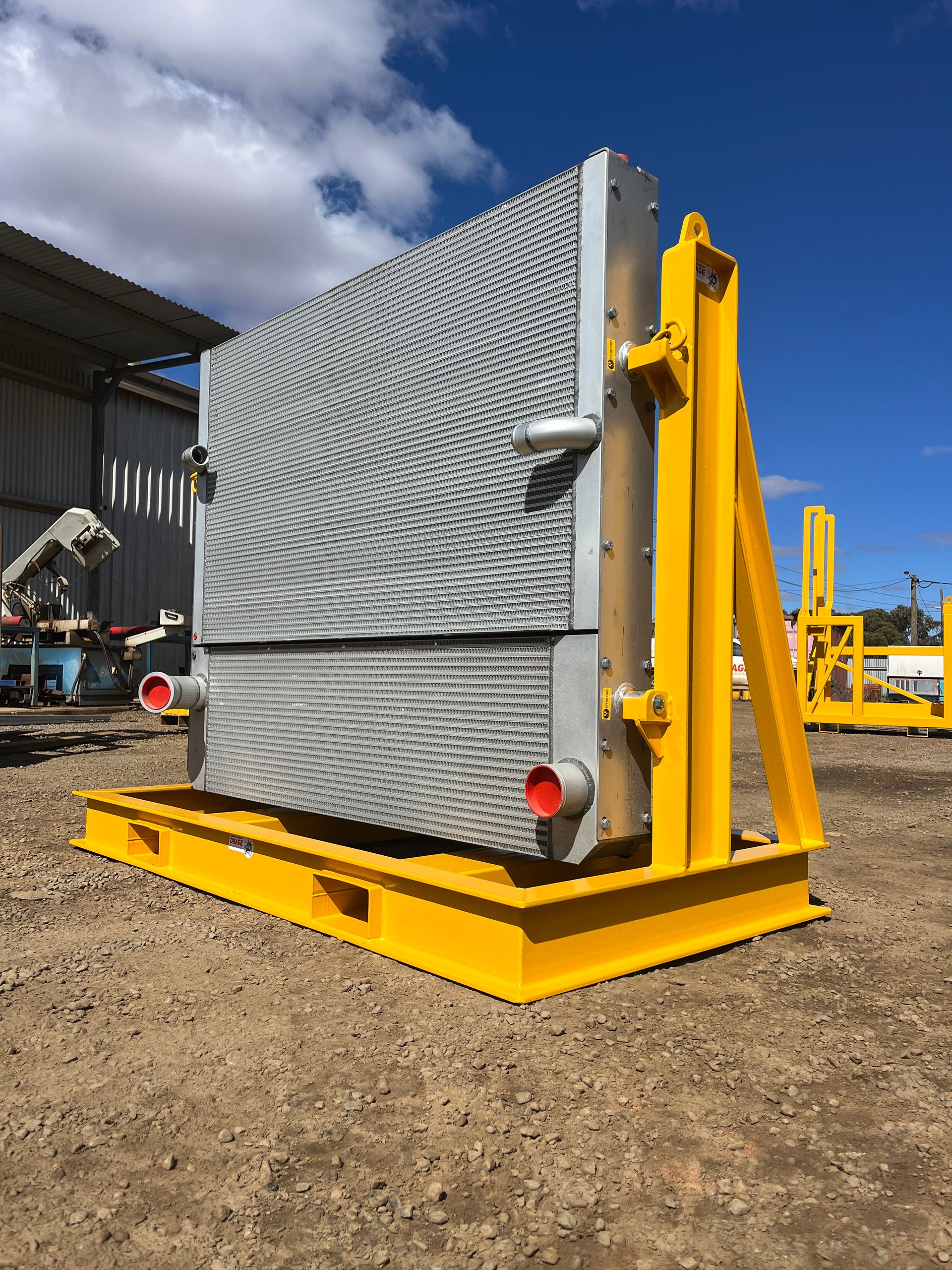 Large, gray industrial radiator mounted on a yellow metal frame outdoors against a blue sky.