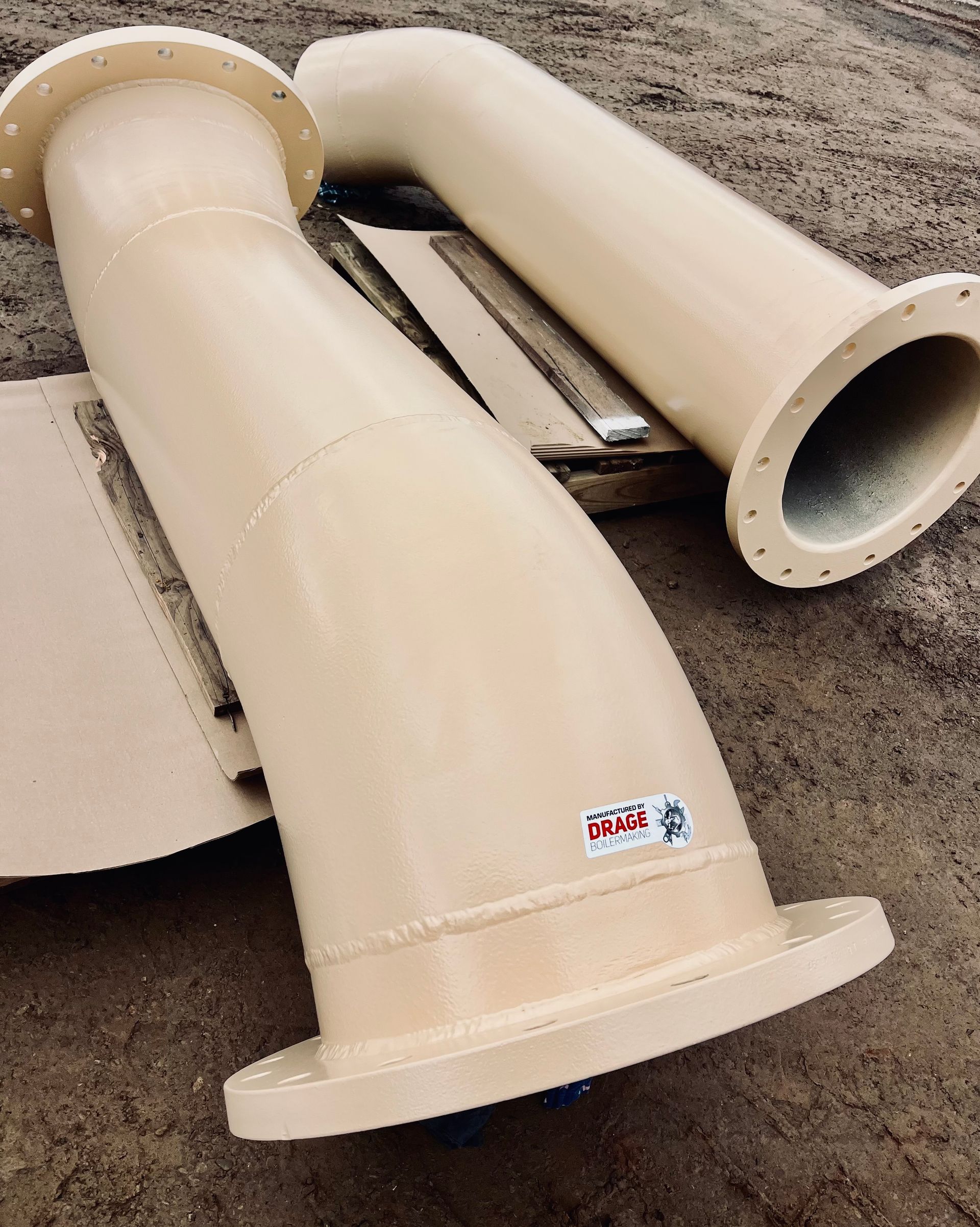 Tan painted metal piping with flanged ends and curved sections, outdoors.