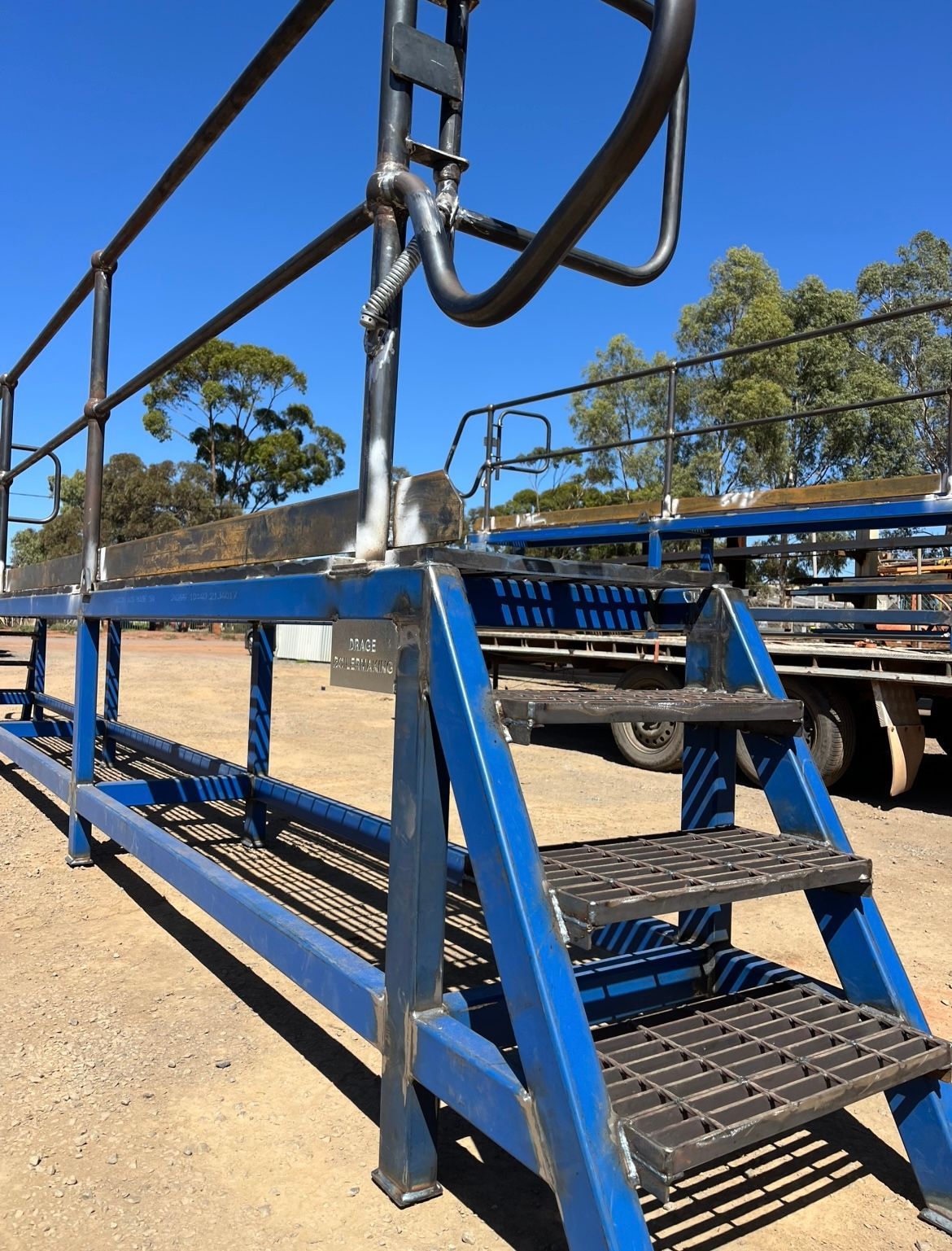 Blue metal access platform with stairs and railing, outdoors on a sunny day.