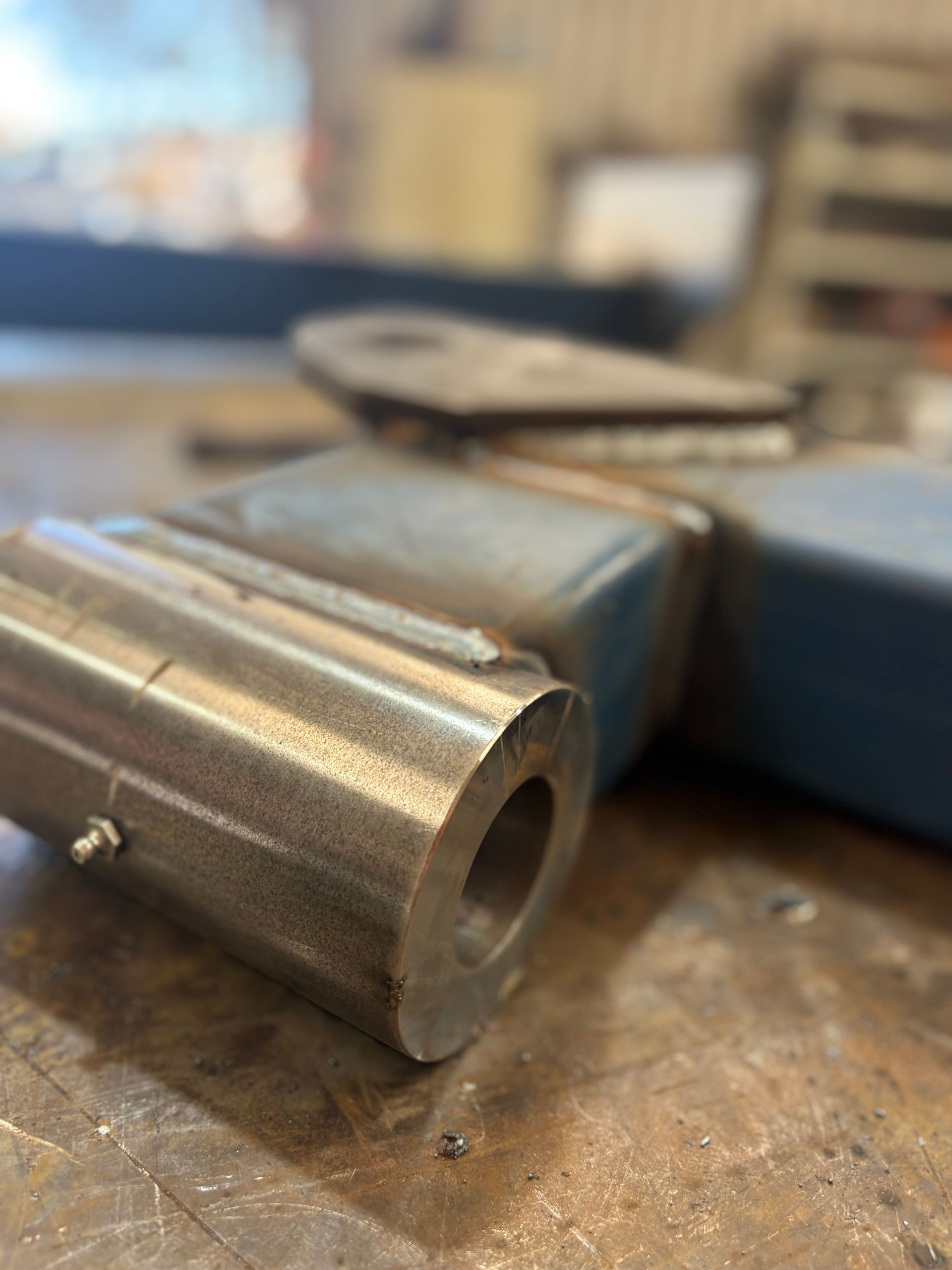 Close-up of a metal industrial component with a cylindrical end and a hole, resting on a work surface.