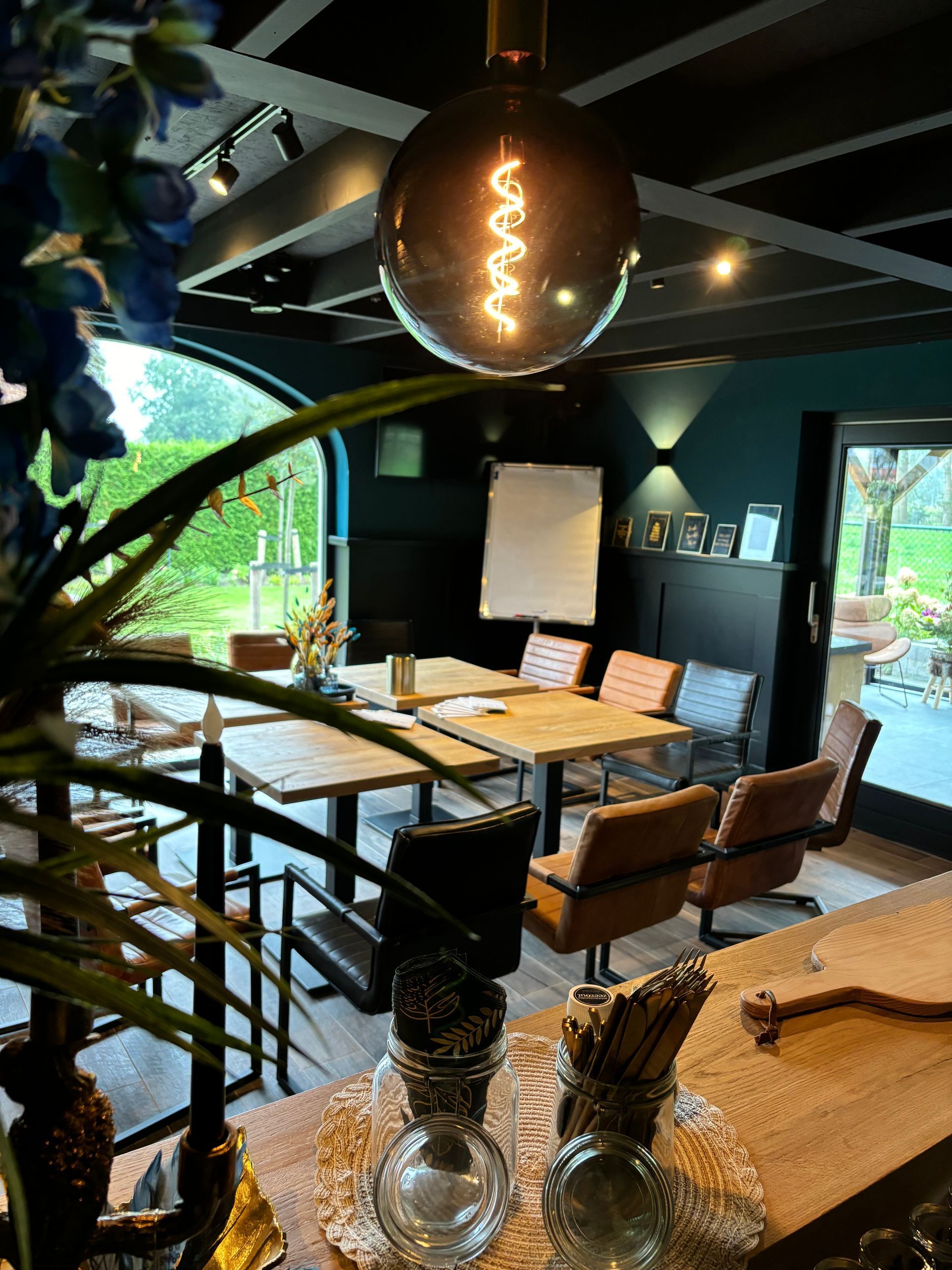 Gezellige ruimte in onze locatie met houten tafels, comfortabele stoelen en een grote hangende bolvormige lamp.