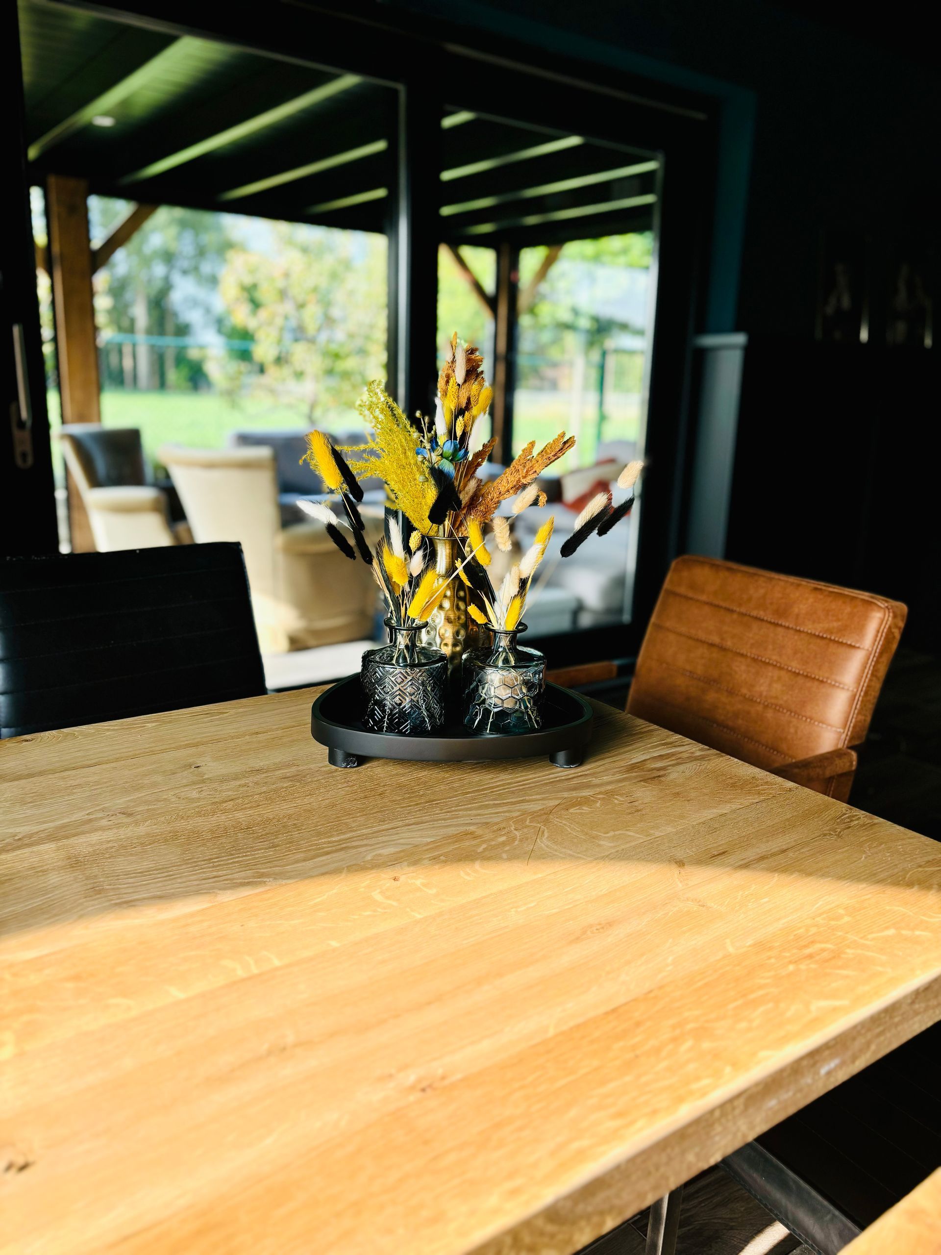 Houten eettafel met een geel bloemstuk in het midden in een moderne openlucht patio.
