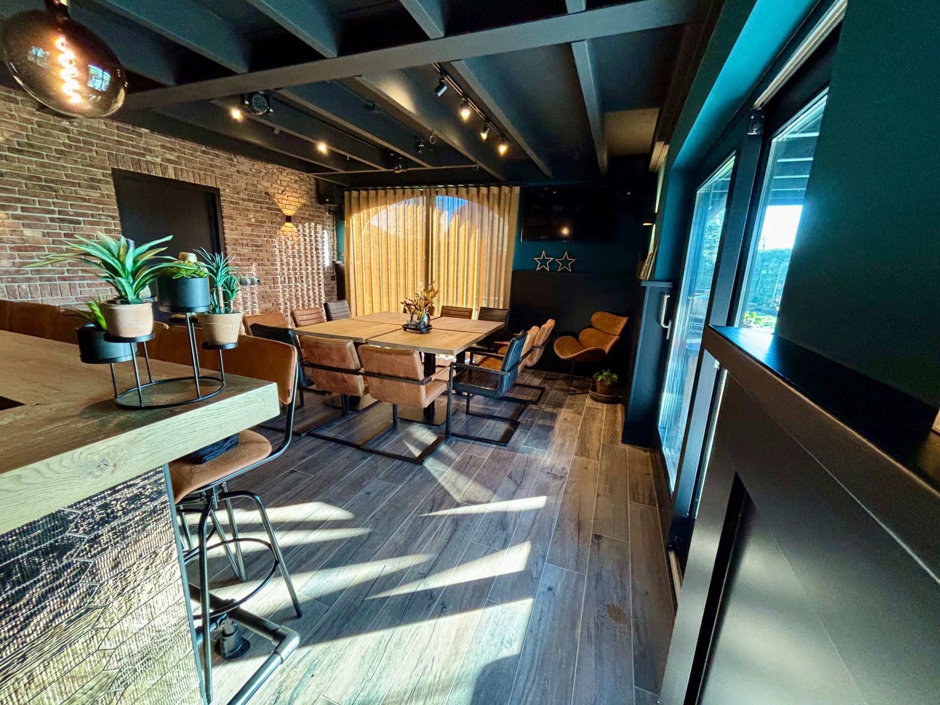 Modern café-interieur met houten tafels en stoelen, bakstenen muren en zonlicht dat door de ramen naar binnen stroomt.