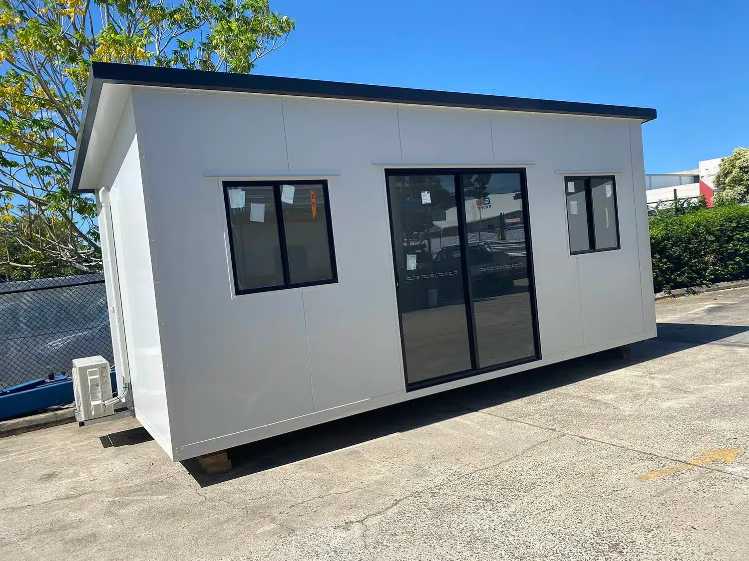 Small white portable office building with black-framed windows and door on a gravel lot.