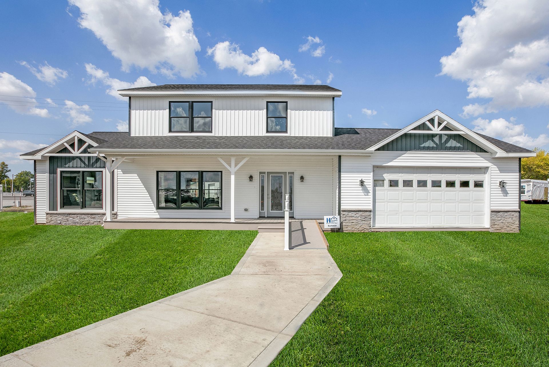 Modern white two-story house with a front porch, garage, and green lawn under a blue sky