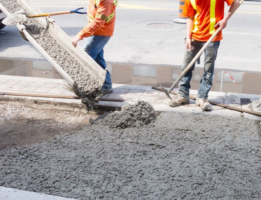 Construction workers pour fresh concrete onto a road repair site.