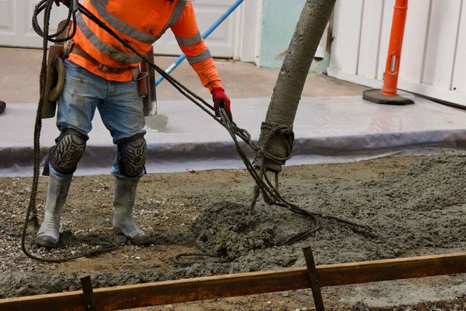 Worker in orange vest pouring concrete with a hose at a construction site