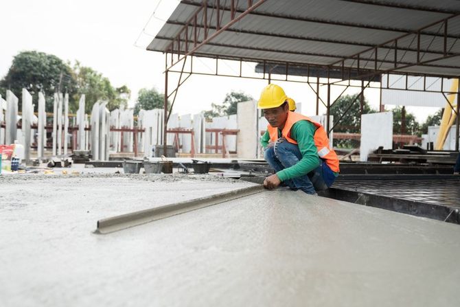 Construction worker smoothing wet concrete on a slab under a metal-roofed structure