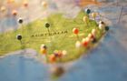 A map of Australia marked with various colorful pushpins, viewed at an angle with selective focus.