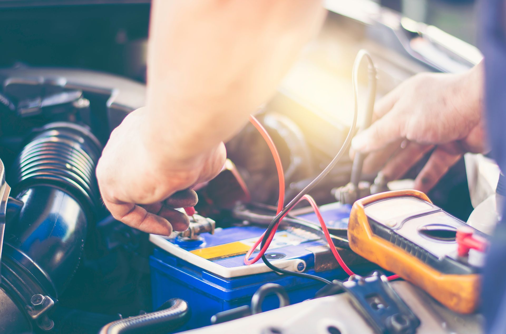 Hands testing car battery with multimeter and jumper cables in an engine bay
