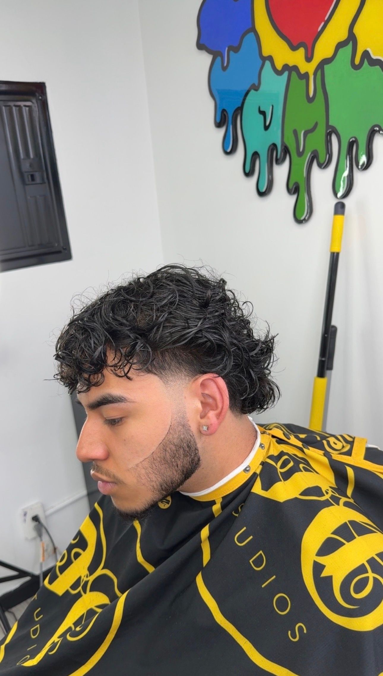 Man getting a haircut, showing a low fade with curly hair. Barber cape in a shop.