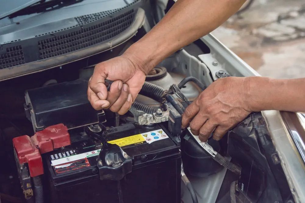 Person's Hands Working on a Car Battery in an Engine Bay; Unscrewing a Terminal — Cool Cars NT in Anula, NT