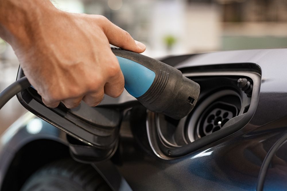 A person's hand holding a blue and black charging nozzle to plug into an electric vehicle port. — Cool Cars NT in Palmerston, NT