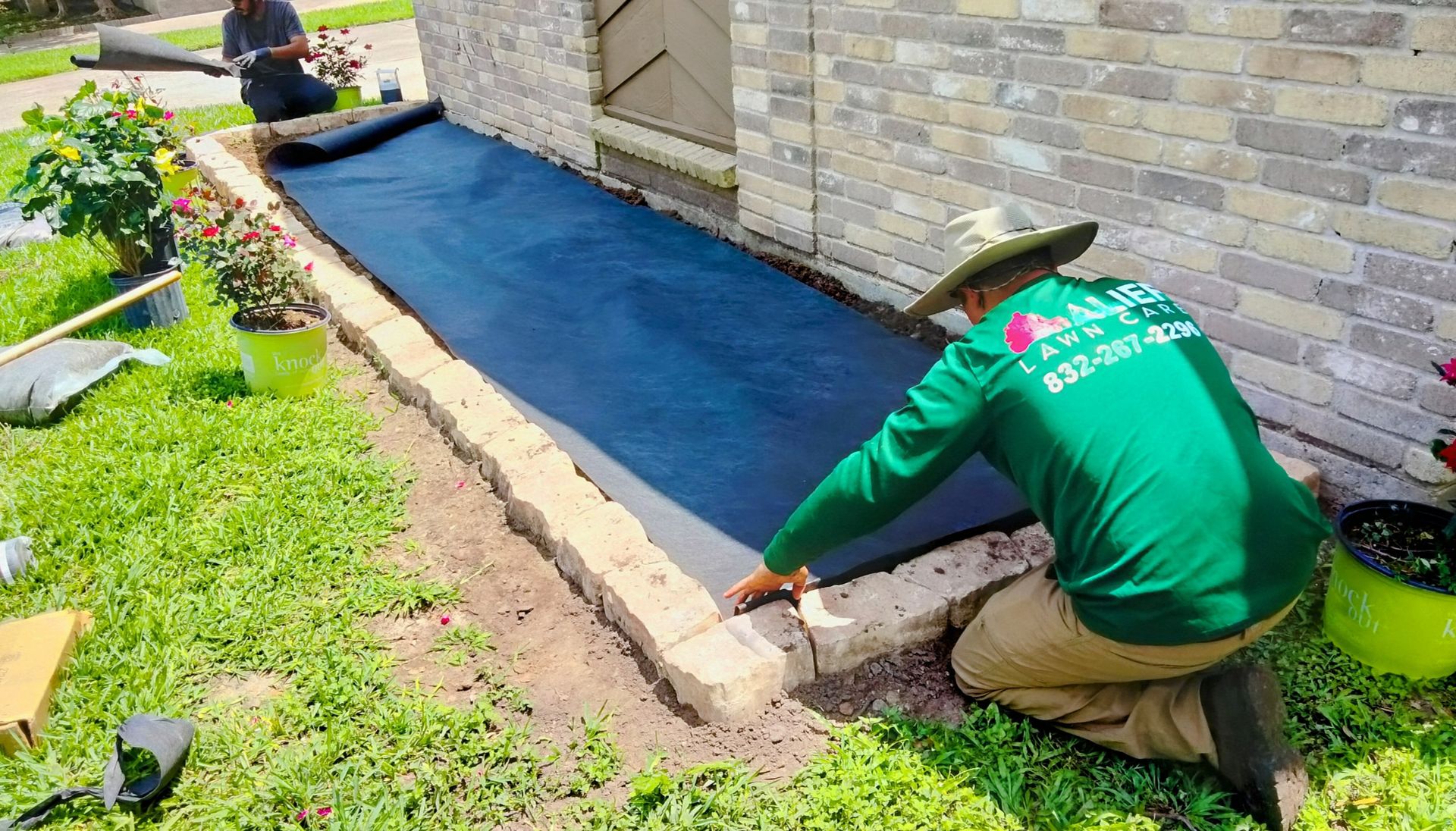 A man is kneeling down in front of a brick building.