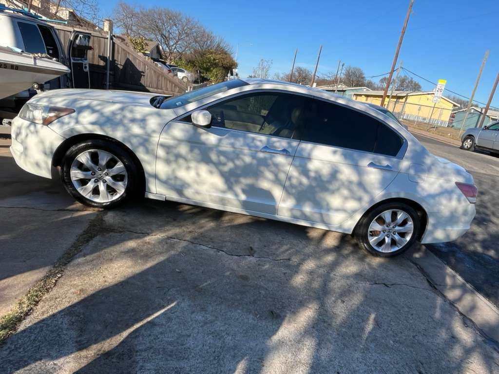 White sedan parked on a sunny street, with tree shadows across the body.
