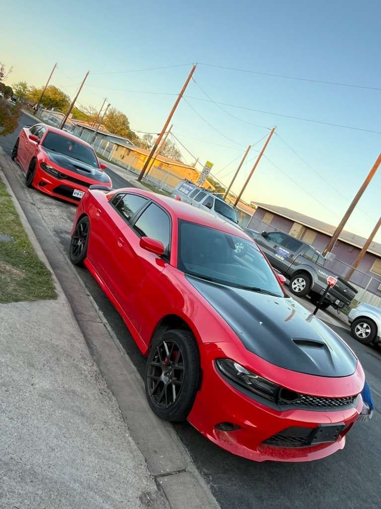 Red sports car parked on a roadside with other cars lined up behind it at sunset.