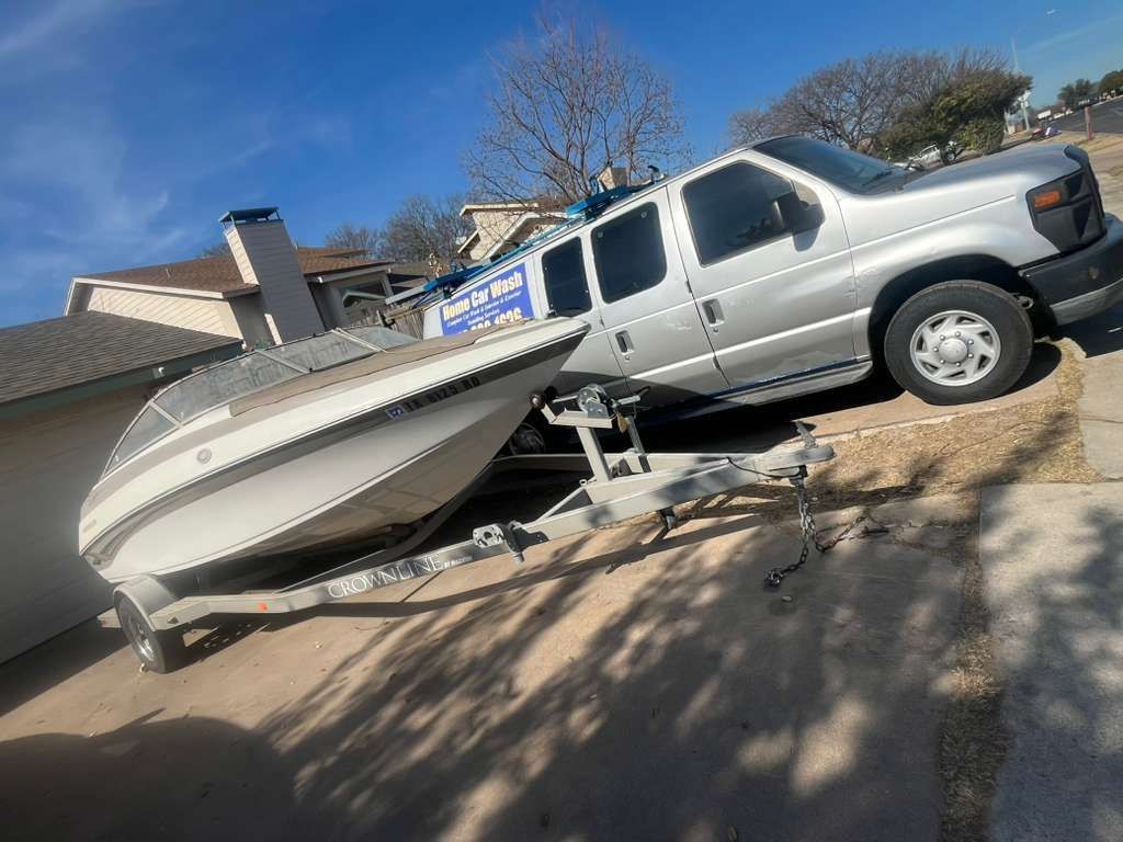 Silver pickup truck towing a white boat on a trailer in a driveway, angled in sunlight