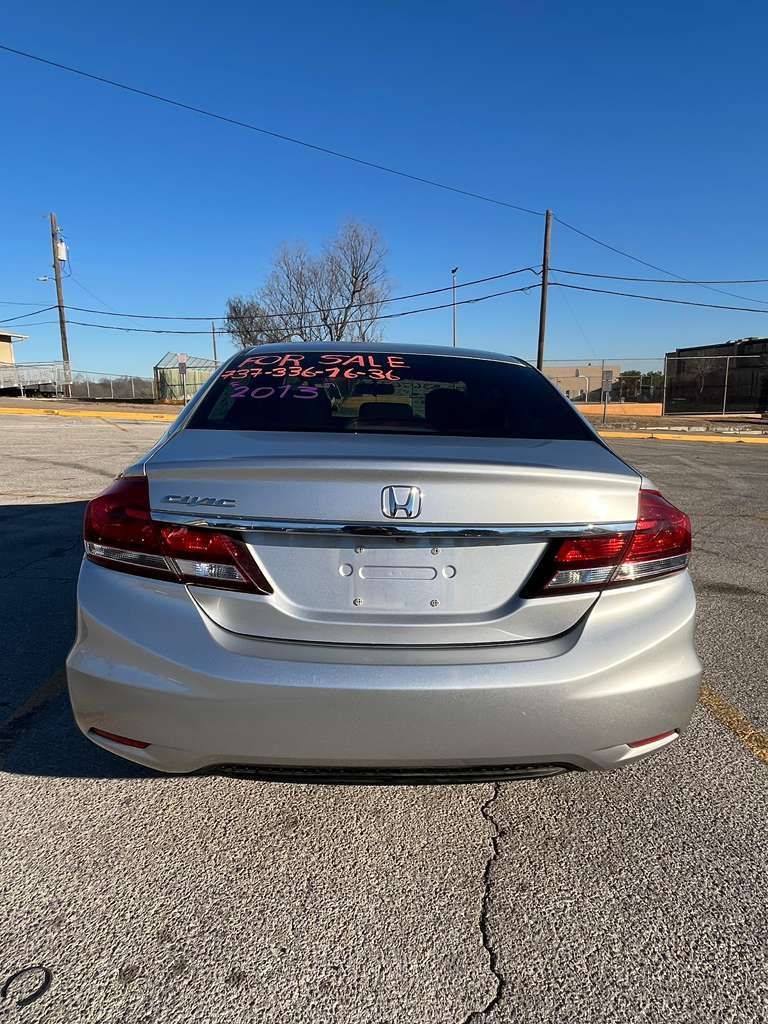Silver Honda sedan parked on cracked pavement under a clear blue sky, rear view.