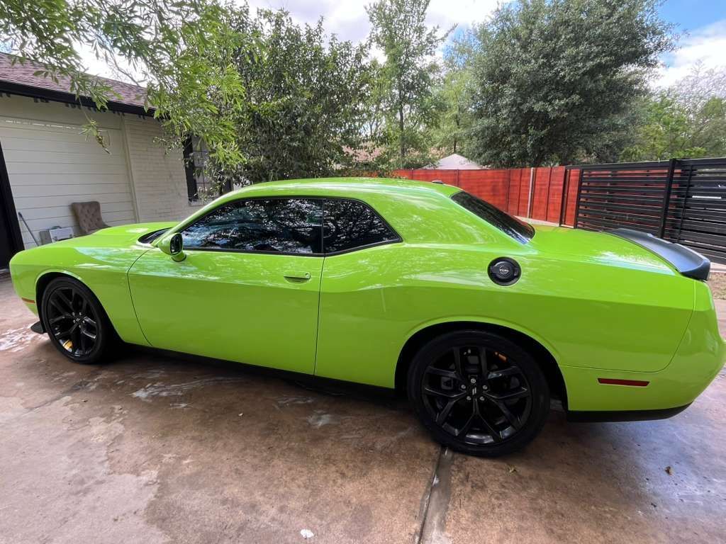 Bright green sports coupe parked on a wet driveway beside a house and red fence