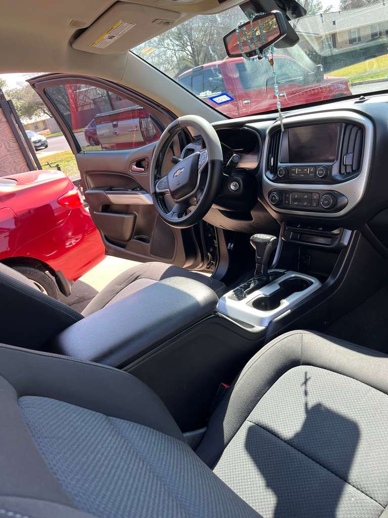 Car interior with black seats, steering wheel, dashboard, and open driver’s door in a red vehicle.