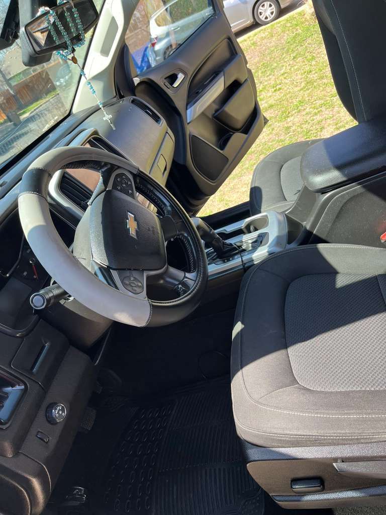 Car interior with black seats, steering wheel, and open driver’s door in sunlight.