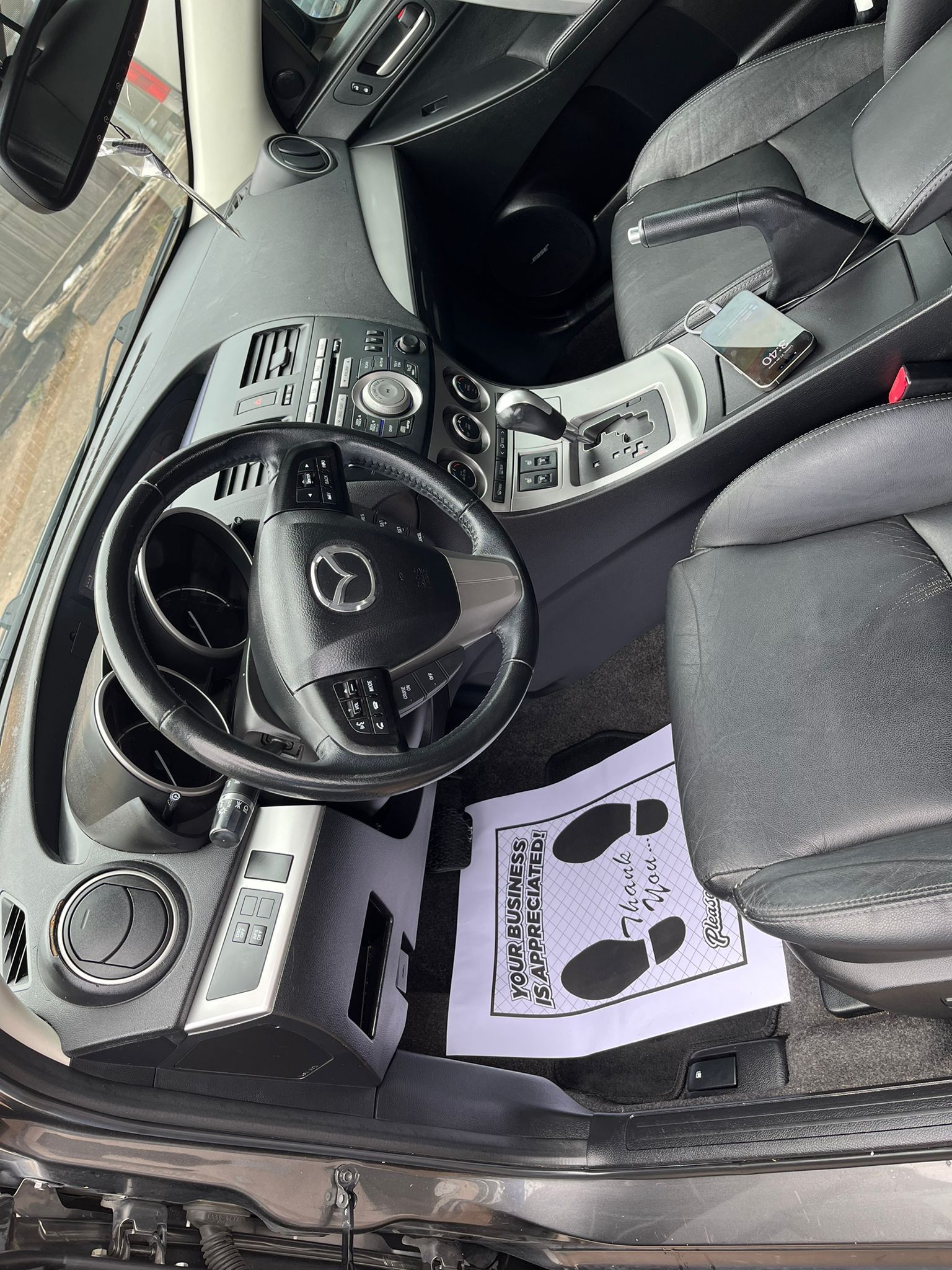 Car interior with black leather seats, steering wheel, dashboard, and floor mat.