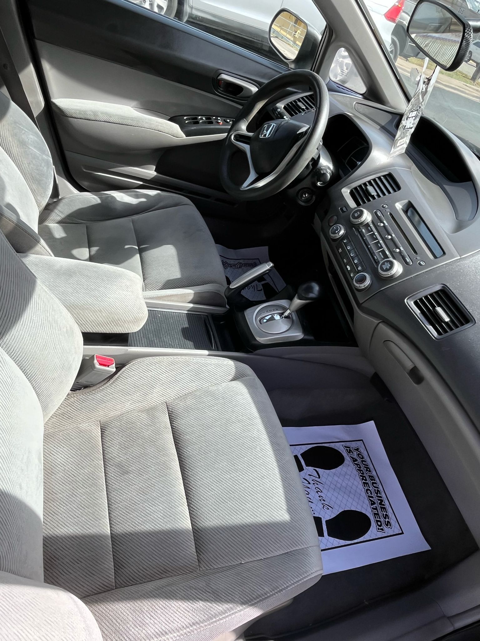 Car interior with gray cloth seats, dashboard, steering wheel, and a sunshade on the passenger floor.