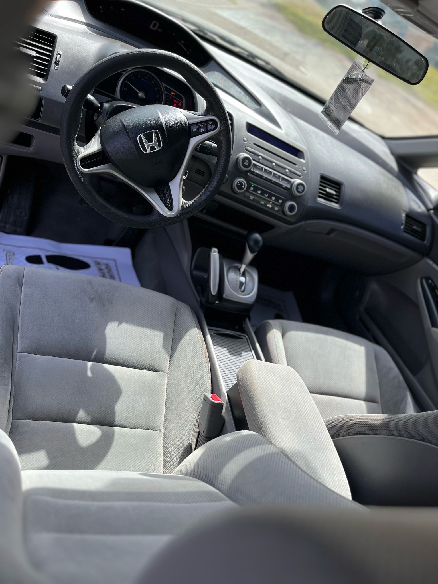 Car interior with gray seats, steering wheel, dashboard, and hanging air freshener in sunlight