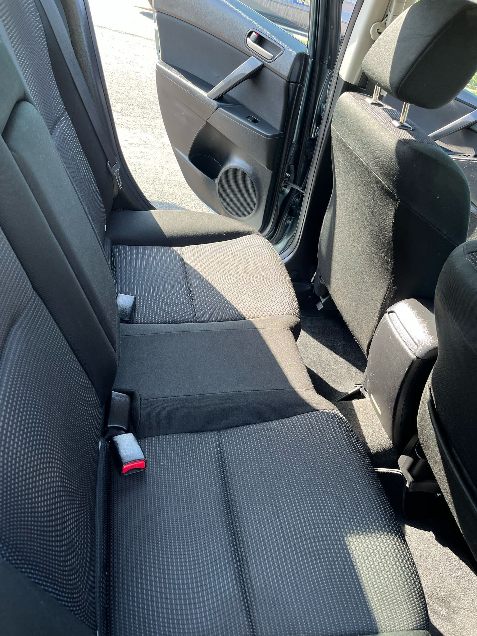 Car back seat with patterned fabric seats, open door, and seat belt visible.