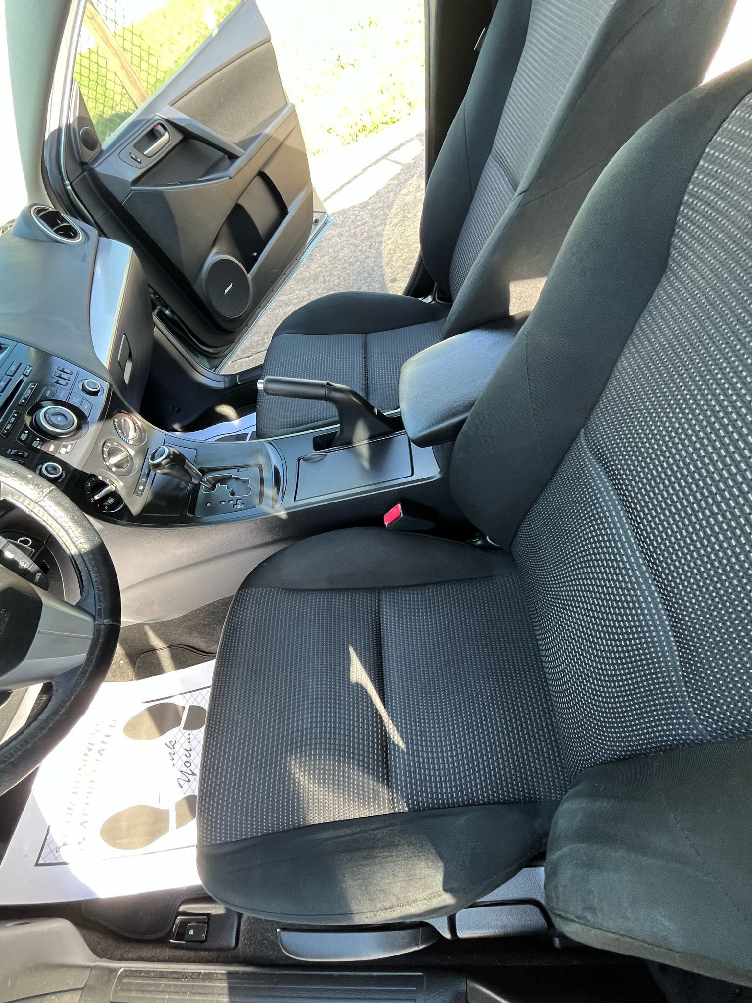 Car interior with front seats, center console, and steering wheel visible; passenger door open.