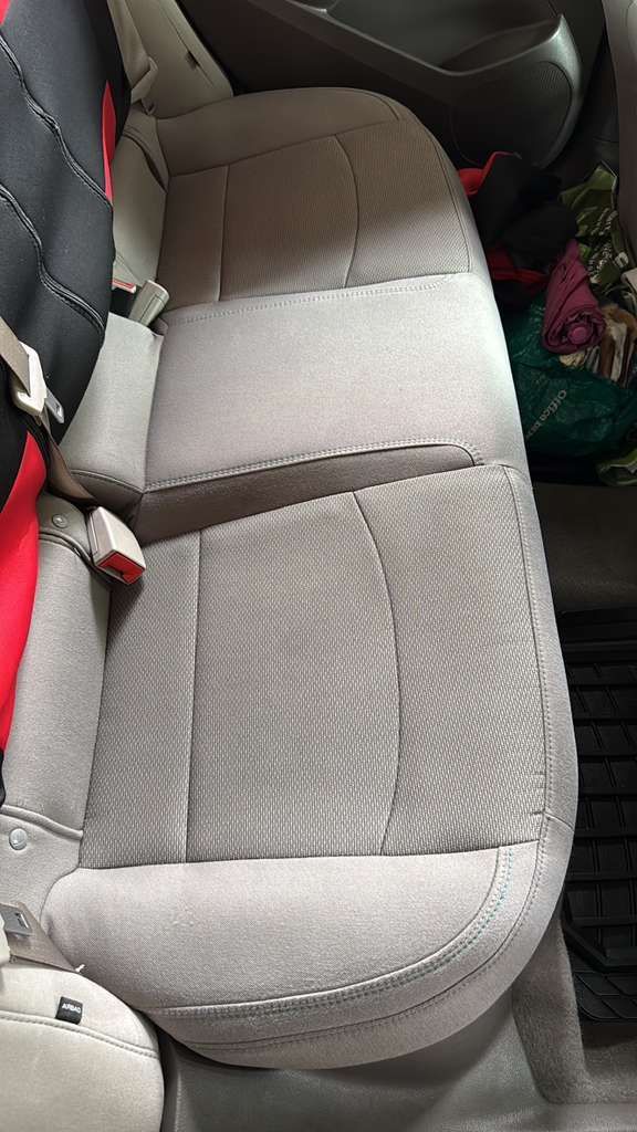 Beige car seat with a gray seat belt across it, seen inside a vehicle.