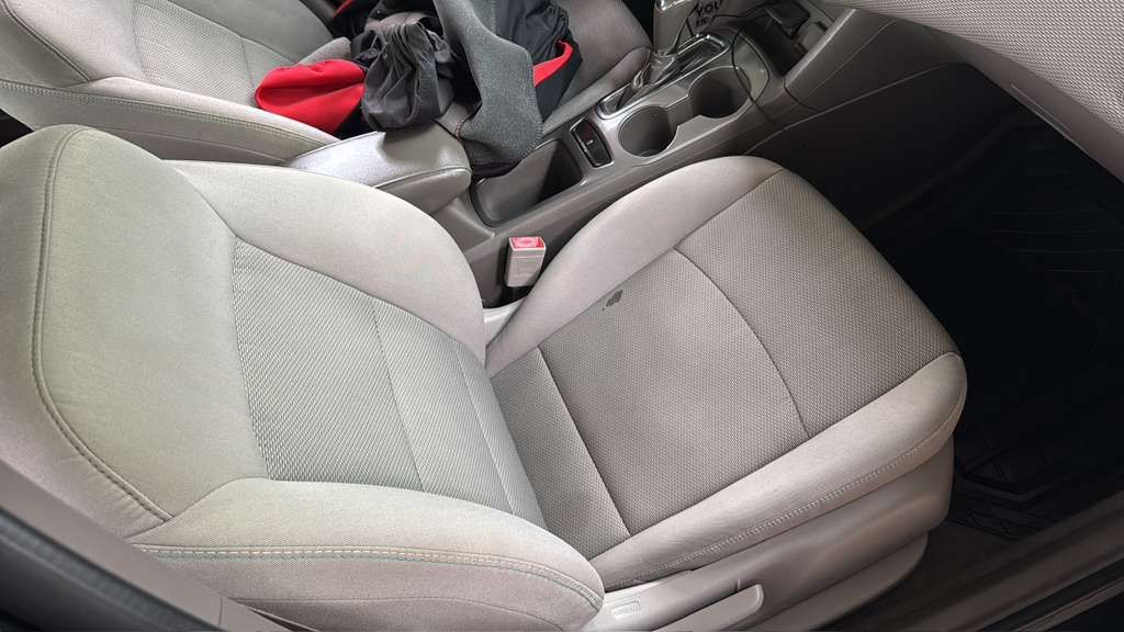 Gray car front seat and center console with visible red seat belts and dark interior