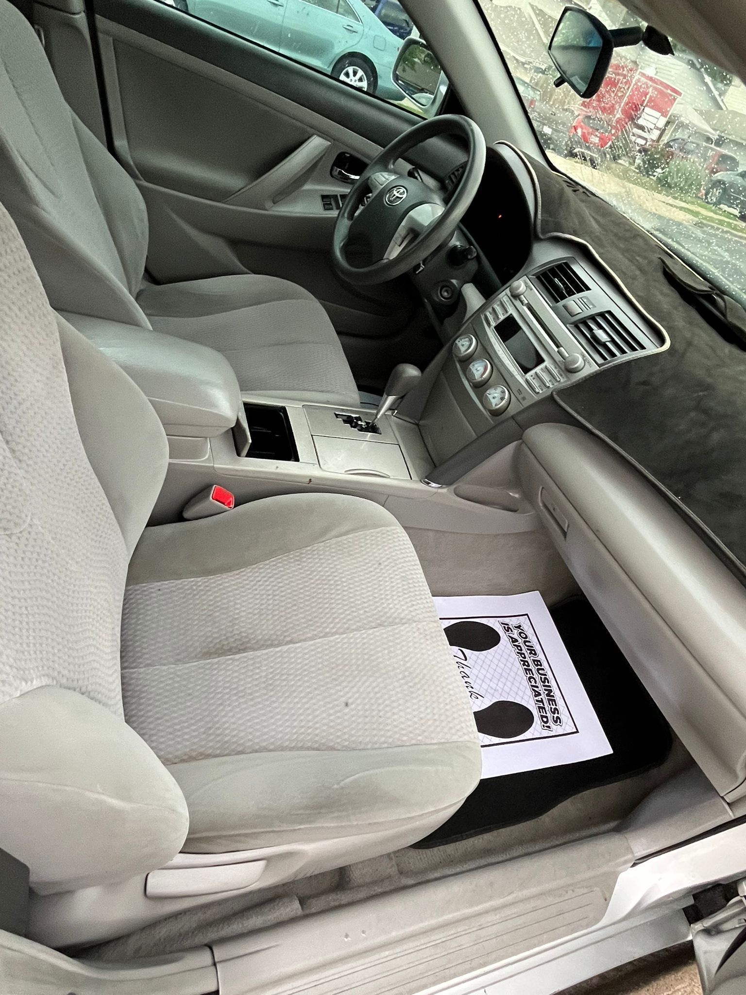 Car interior with beige seats, center console, and a black-and-white card on the passenger floorboard.