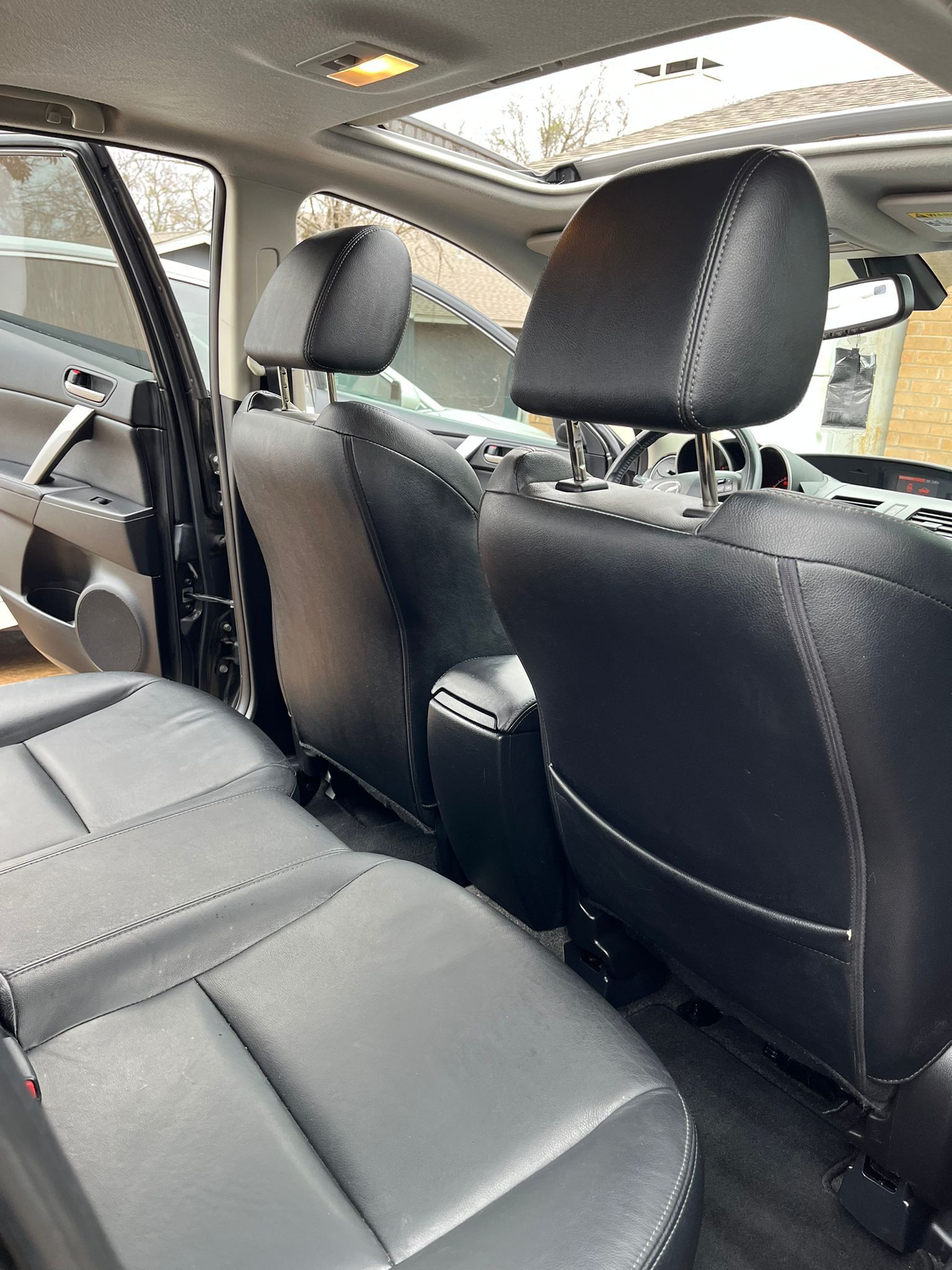 Inside a car, showing black leather seats and headrests with the rear door open.