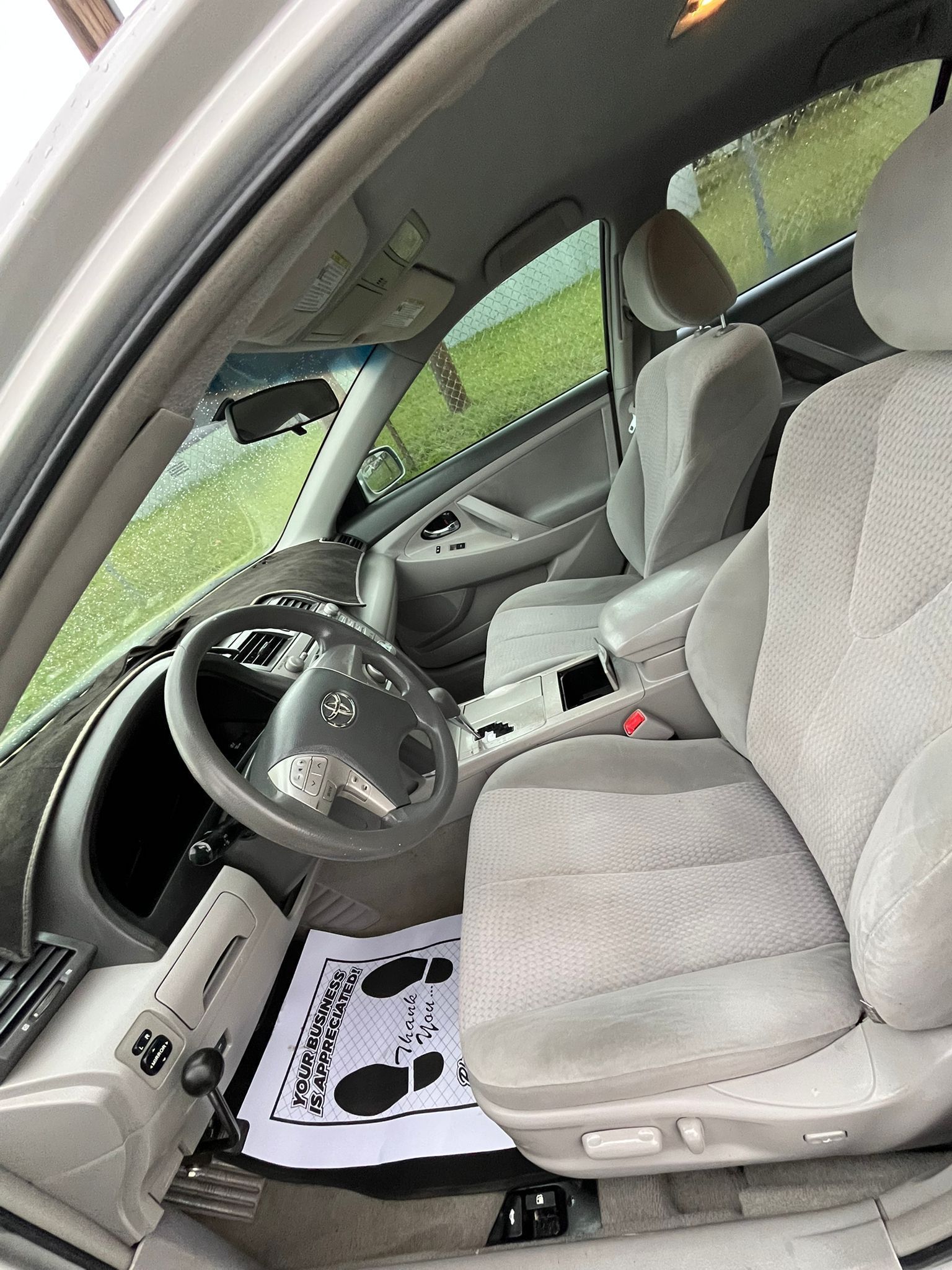 Car interior with gray seats, steering wheel, and black-and-white floor mat, viewed from the open driver door