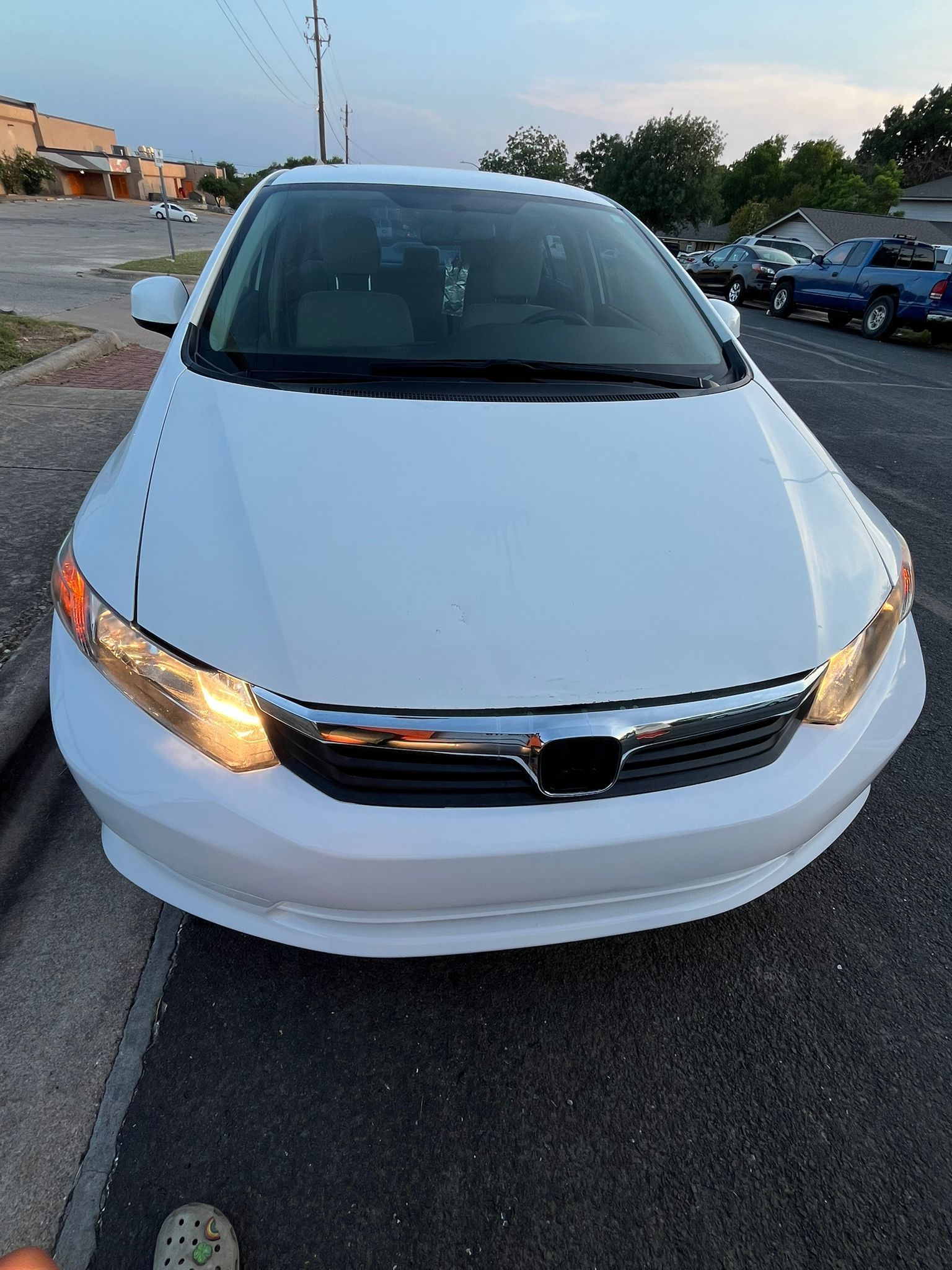 White sedan parked on a street at dusk with headlights on