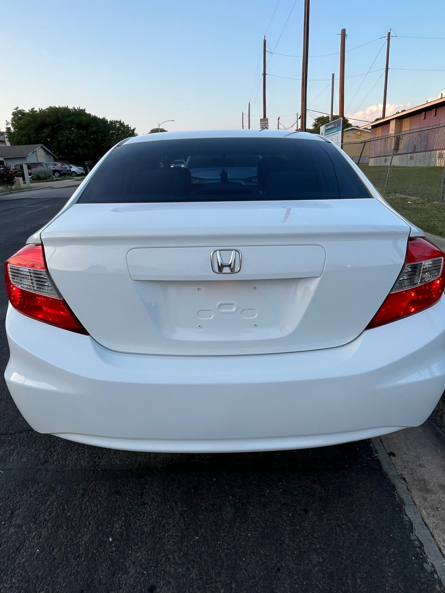 Rear view of a white Honda sedan parked on a roadside at dusk