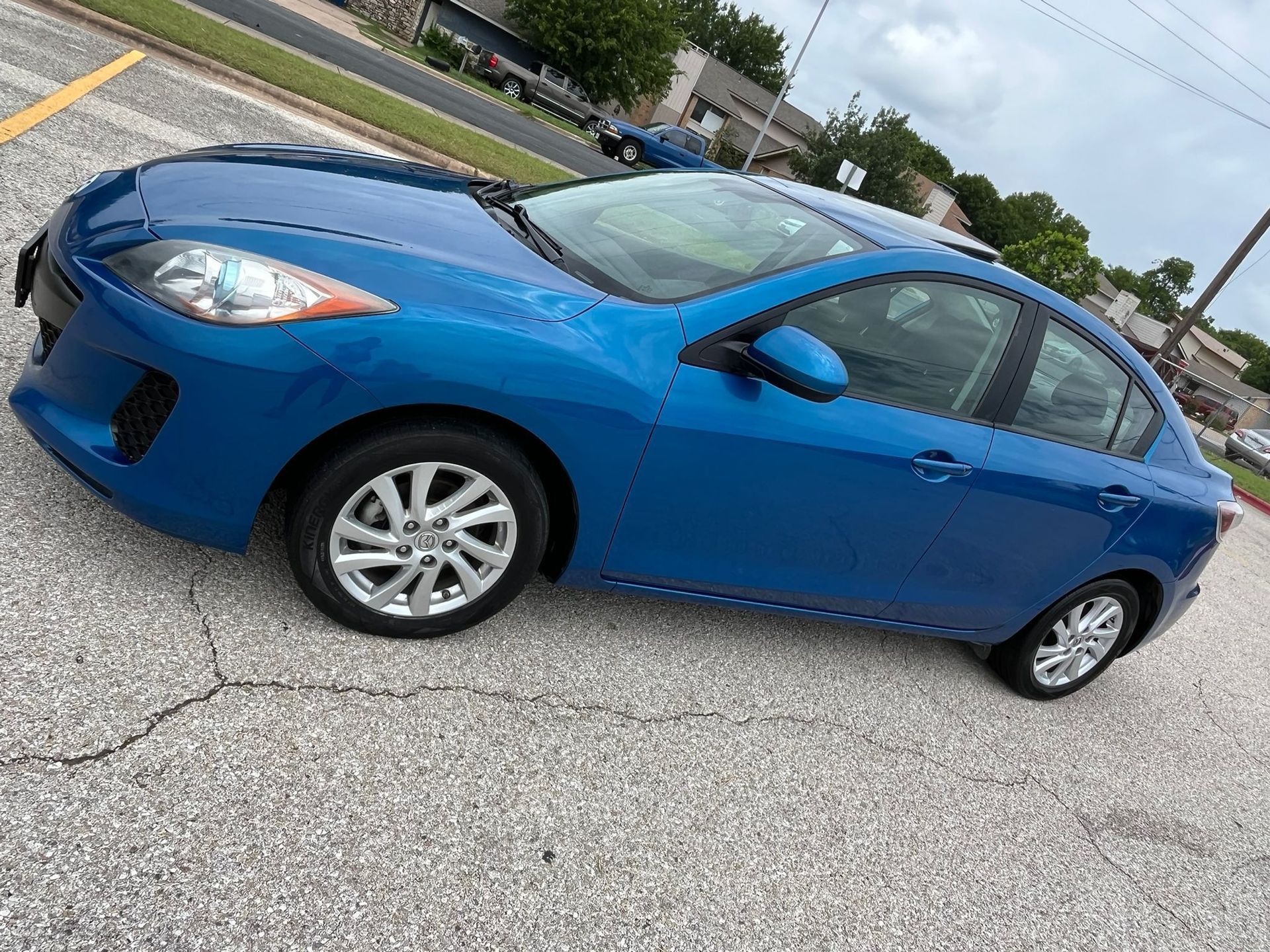 Blue sedan parked on a cracked asphalt lot, angled side view.