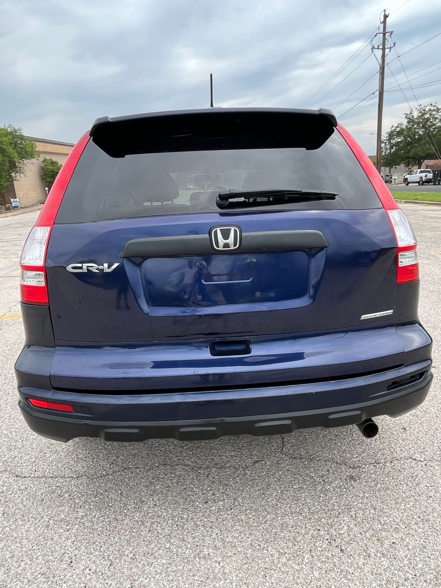 Rear view of a dark blue Honda CR-V parked on a gravel lot under a cloudy sky