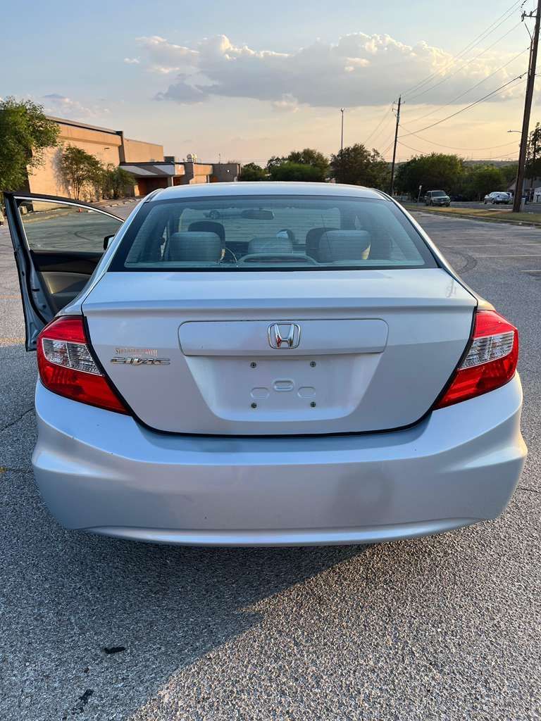 Rear view of a silver Honda sedan with the driver’s door open, parked outdoors at sunset.